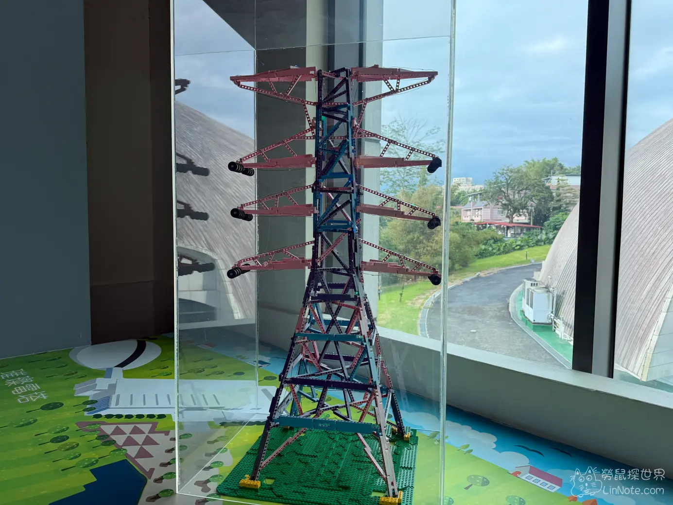 窗邊由積木組裝的輸電鐵塔模型與戶外綠景