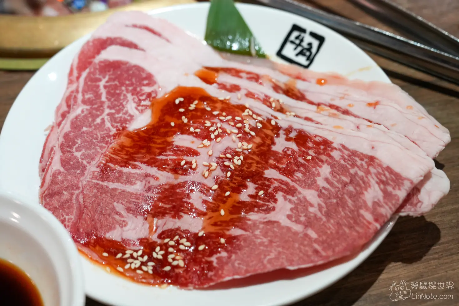 白色圓盤盛裝淋有醬汁與白芝麻的薄切肉片