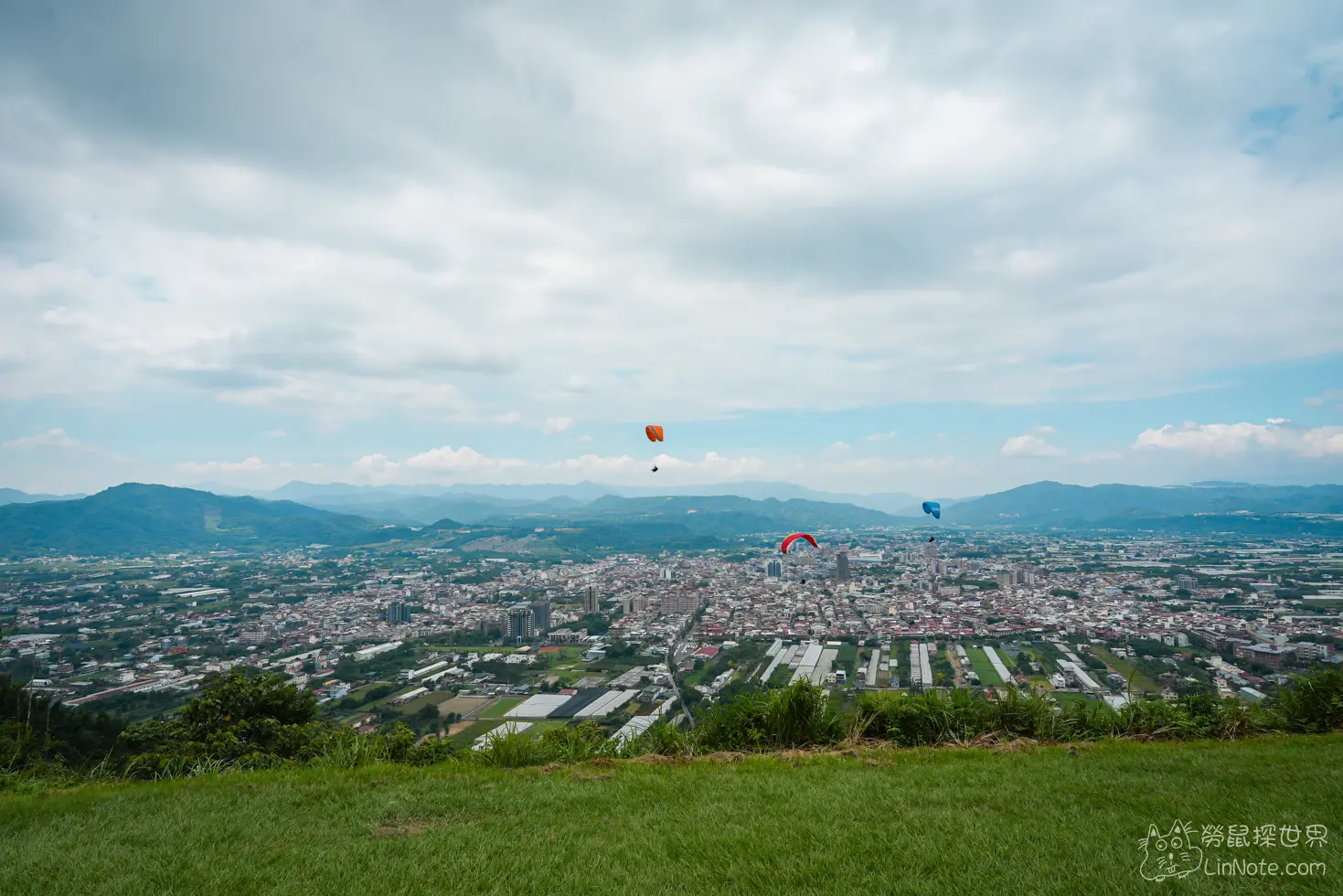 三具不同顏色的飛行傘飄浮在城鎮與群山上空的壯闊景致