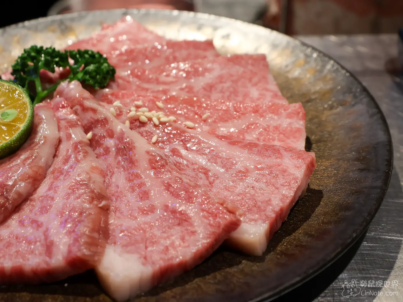 黑色圓盤上油花細緻並撒上白芝麻的安格斯牛小排生肉片