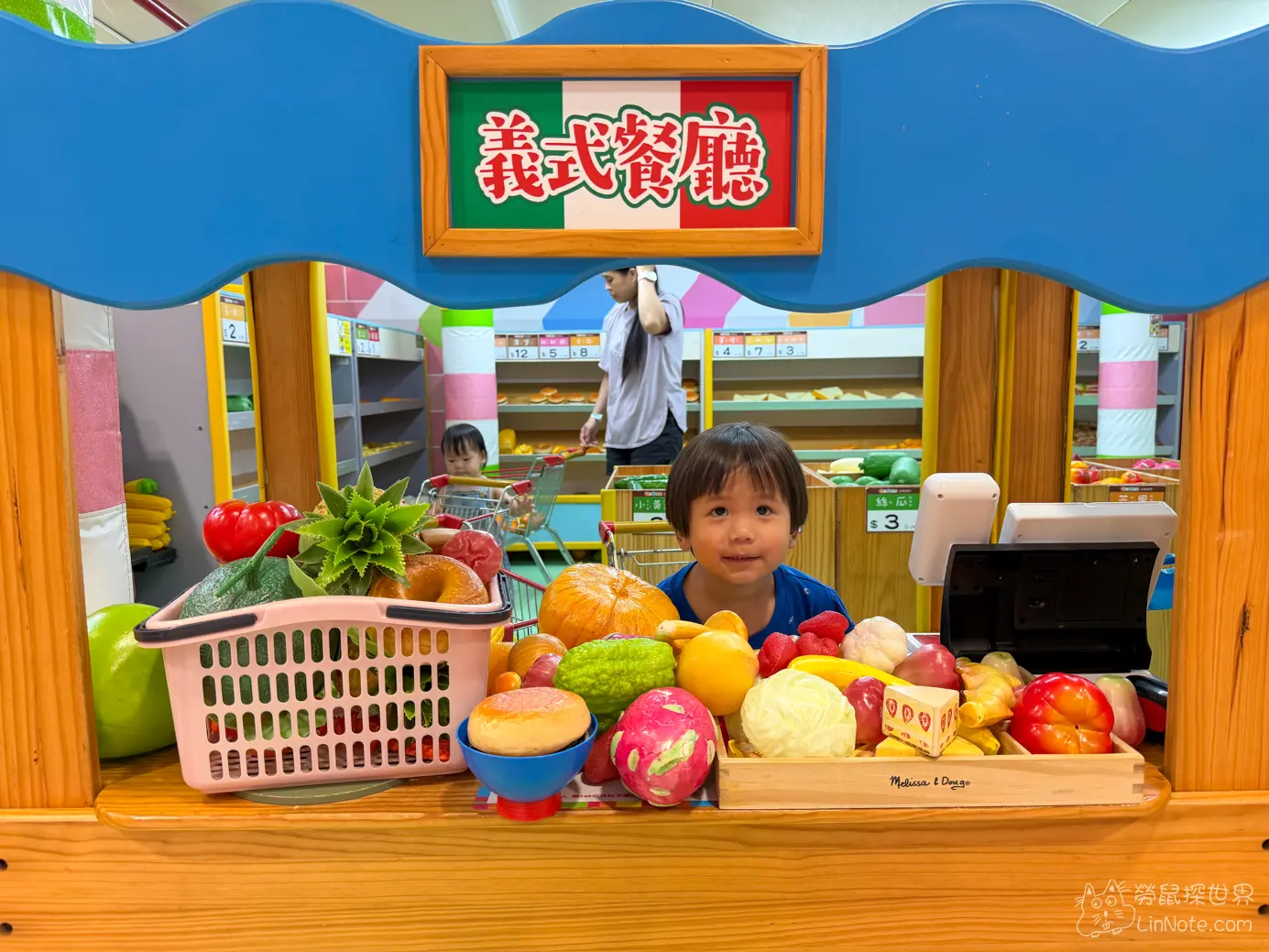 幼童在義式餐廳木質櫃台前擺放玩具蔬果