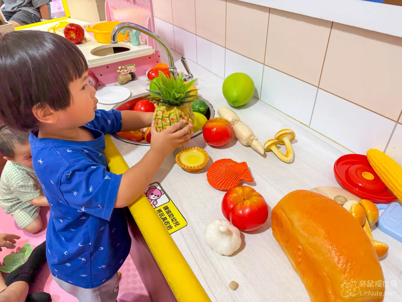 幼童在仿真廚房流理台前把玩具鳳梨放入水槽