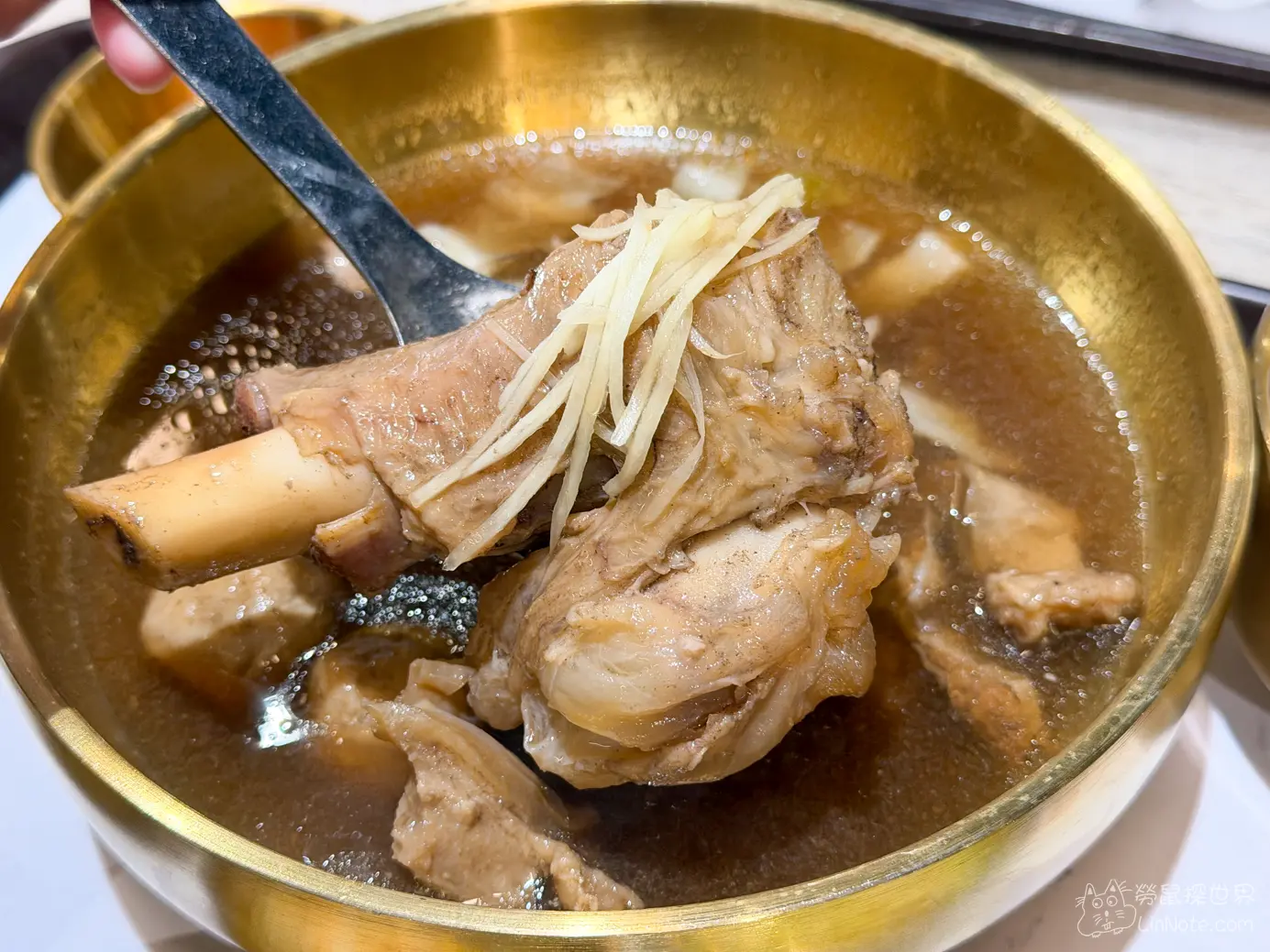 金屬湯匙舀起孔明羊綜合湯中的帶骨羊肉塊與薑絲