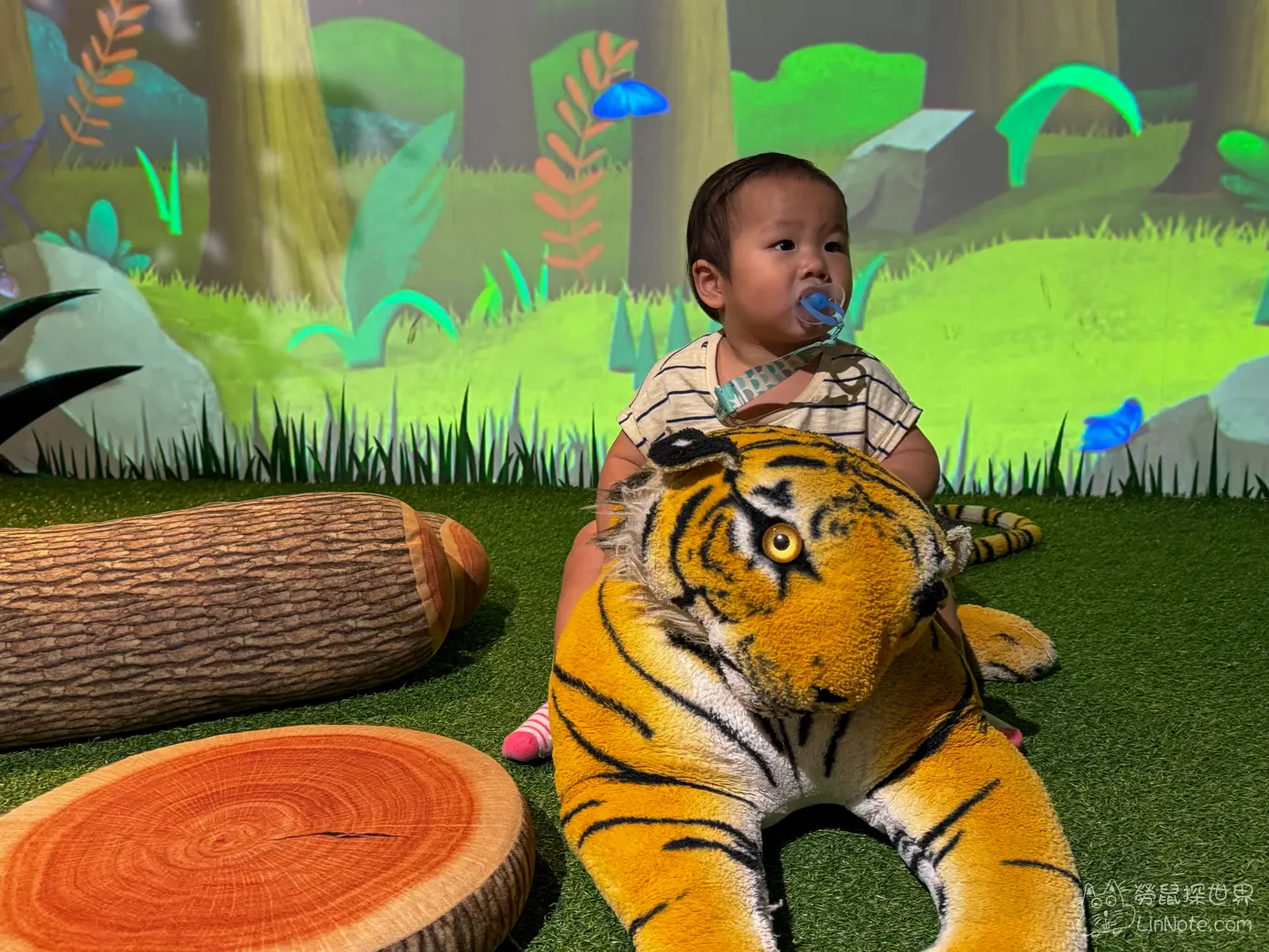 草皮造景上的大型老虎玩偶與周圍仿木頭造型軟墊道具