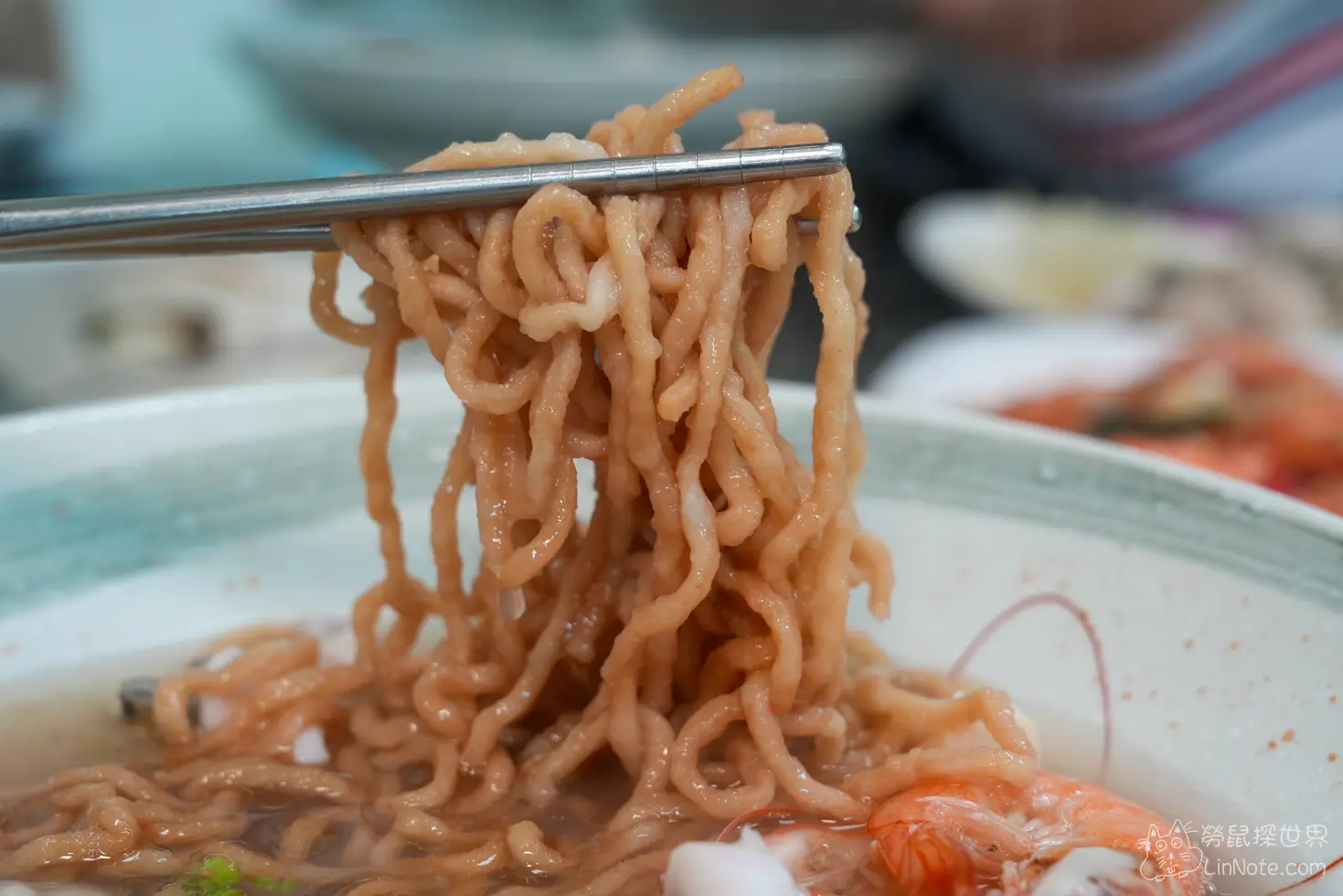 用金屬筷子夾起吸飽海鮮高湯的捲曲鍋燒意麵特寫